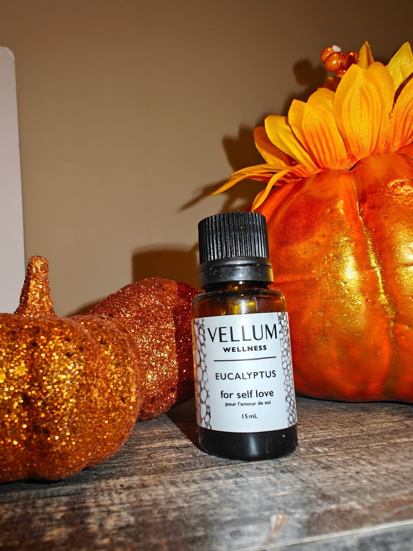 Vellum Wellness Eucalyptus oil bottle with decorative pumpkins on a wooden surface